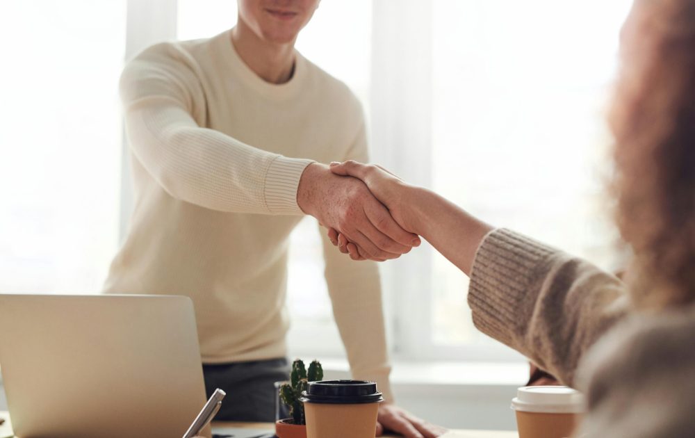 Close-up of professionals shaking hands over coffee in a modern office.