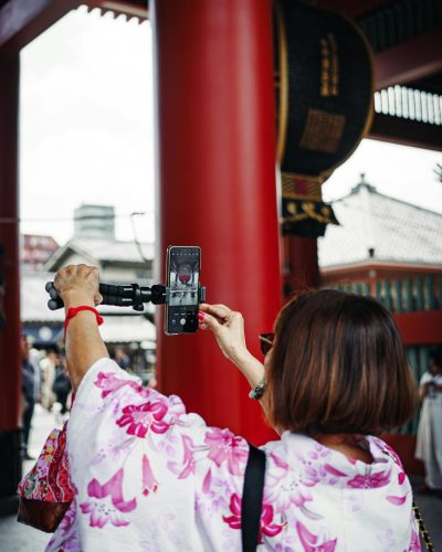 A woman in a floral kimono takes a selfie with a smartphone at Senso-ji Temple in Tokyo, Japan.
