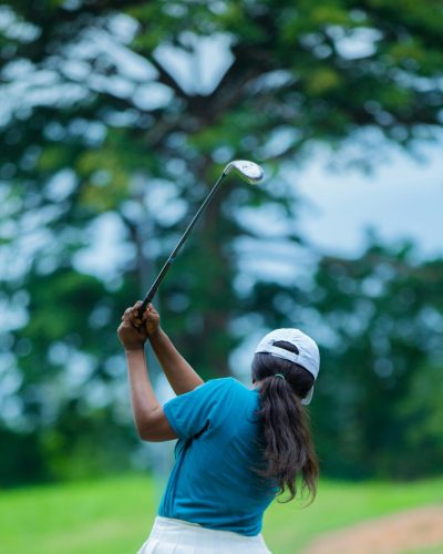 Woman swings golf club on a vibrant green course on a sunny day.