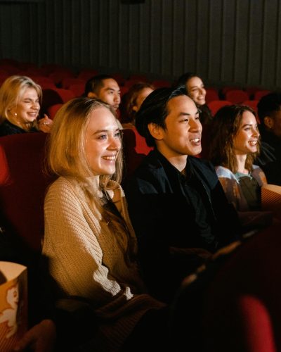 A diverse group of friends enjoying a movie at the cinema, with smiles and popcorn.